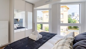 Un dormitorio con cama, armario y vistas a edificios a través de amplios ventanales.