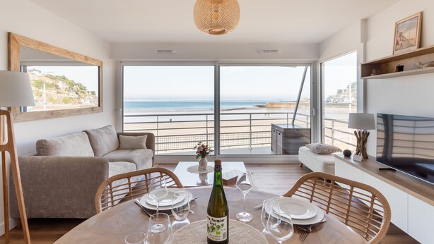 Un comedor con una mesa preparada para dos personas, una botella de vino y vista a la playa.