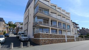 Un edificio de varios pisos con balcones, base de piedra y un estacionamiento con automóviles.