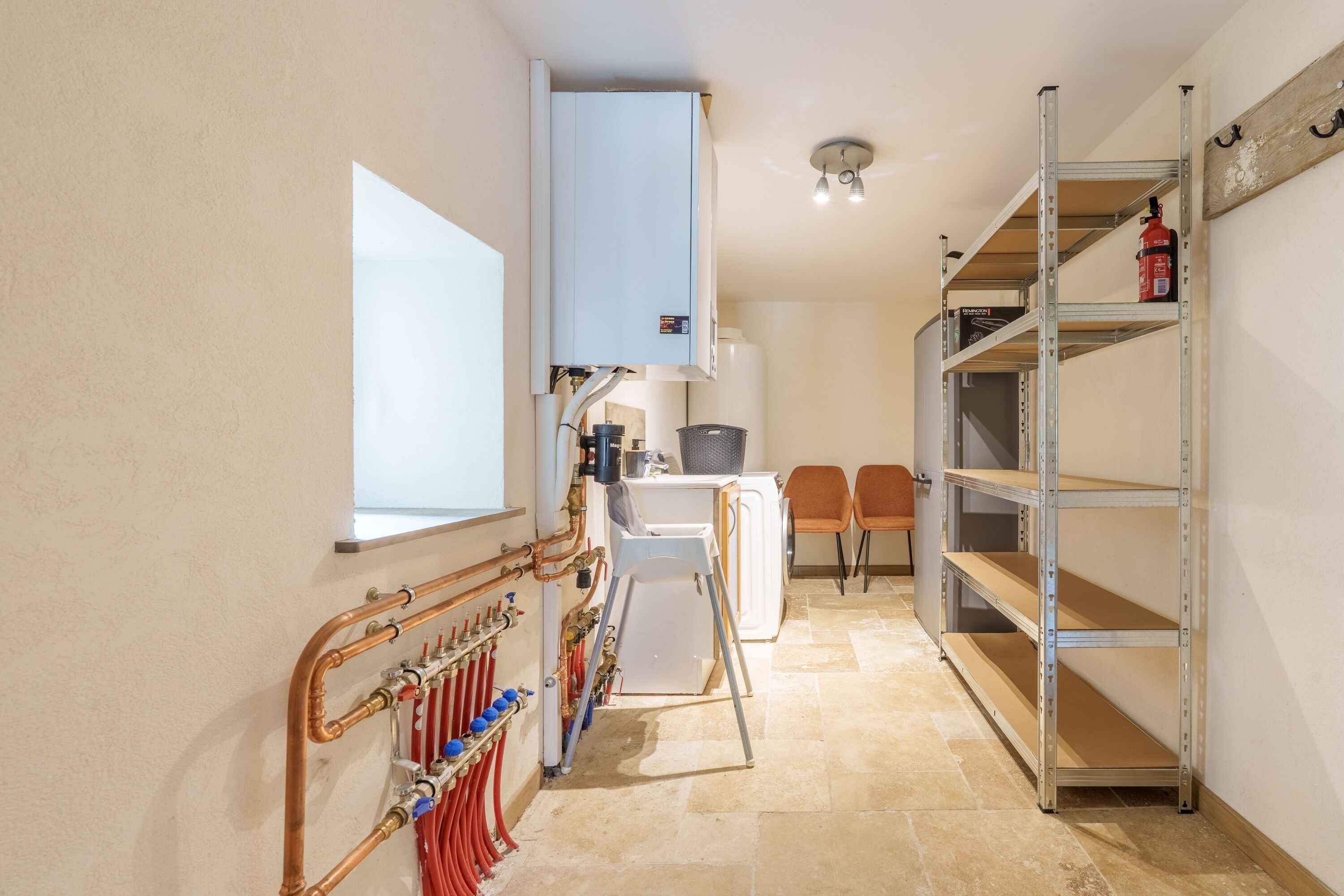 A narrow hallway with a radiator, a white washing machine, and a metal shelving unit with a fire extinguisher.