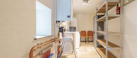 A narrow hallway with a radiator, a white washing machine, and a metal shelving unit with a fire extinguisher.