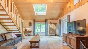 A spacious living room with a wooden staircase, a large window, a wooden coffee table, a sofa, a TV, and a cabinet.