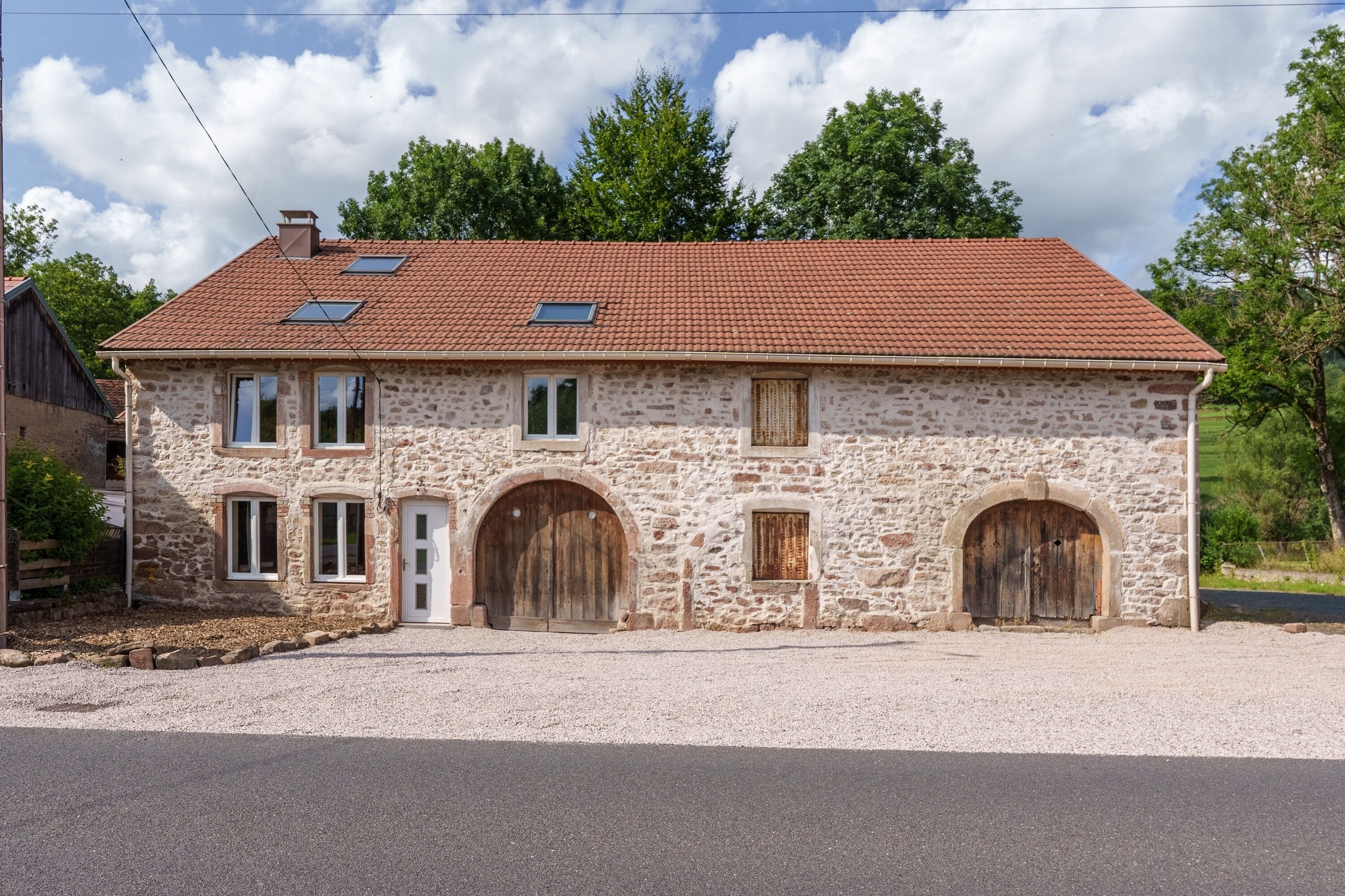 A stone building with a red-tiled roof, two windows with shutters, and a wooden door.