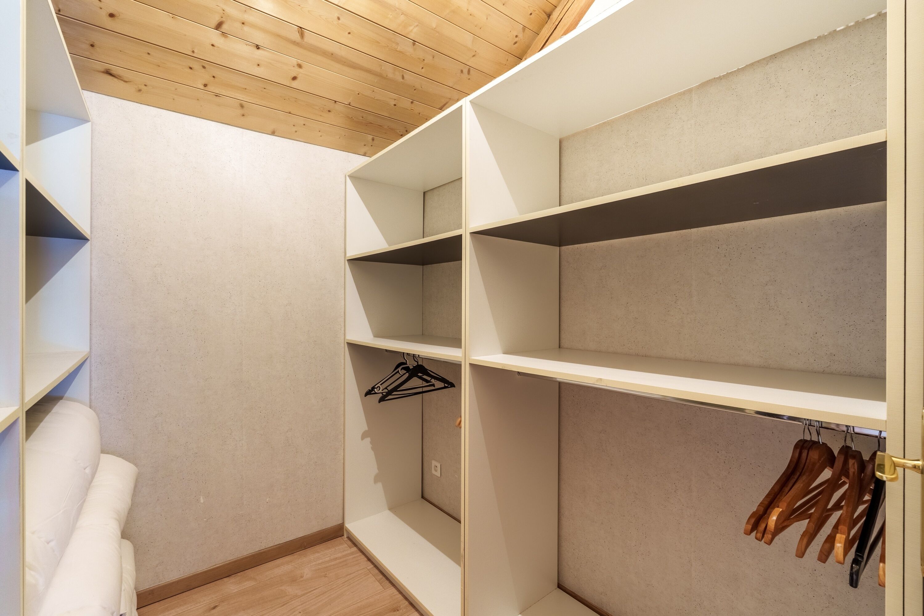 Vestidor amplio con estantes abiertos y espacio para colgar, techo de madera y paredes de color claro.