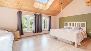 A bedroom with a skylight, a bed, a bedside table, and a window with curtains.
