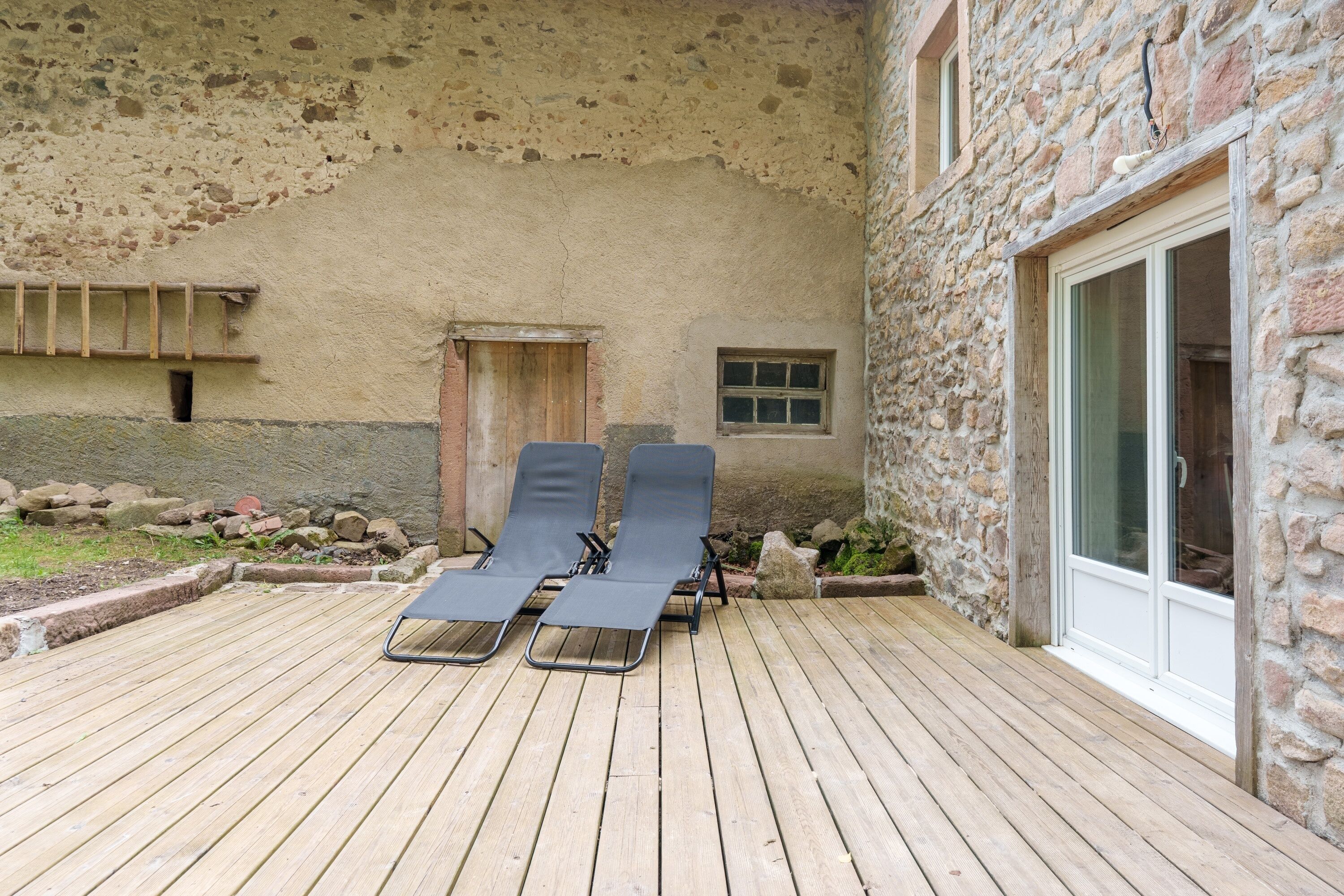 Een houten terras met twee lounge stoelen, een stenen muur en een raam met uitzicht.
