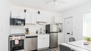 Una cocina moderna con electrodomésticos de acero inoxidable, armarios blancos y una zona de comedor con mesa y sillas.