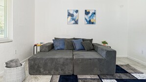 Un sofá seccional gris con cojines azules y grises, una pequeña mesita con una planta y arte abstracto en la pared.