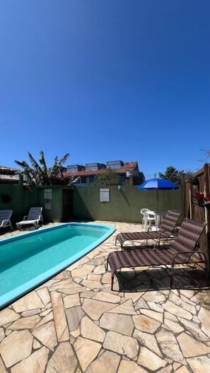A swimming pool with lounge chairs and a stone patio. - Pousada Recanto do Rosa (Imbituba)