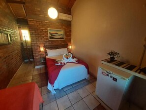 A room with a bed, a small refrigerator, a brick wall, and a painting. - Pousada Recanto do Rosa (Imbituba)