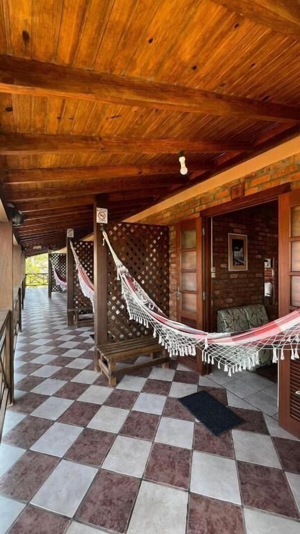 A covered porch with a checkered floor, wooden beams, and a hammock. - Pousada Recanto do Rosa (Imbituba)