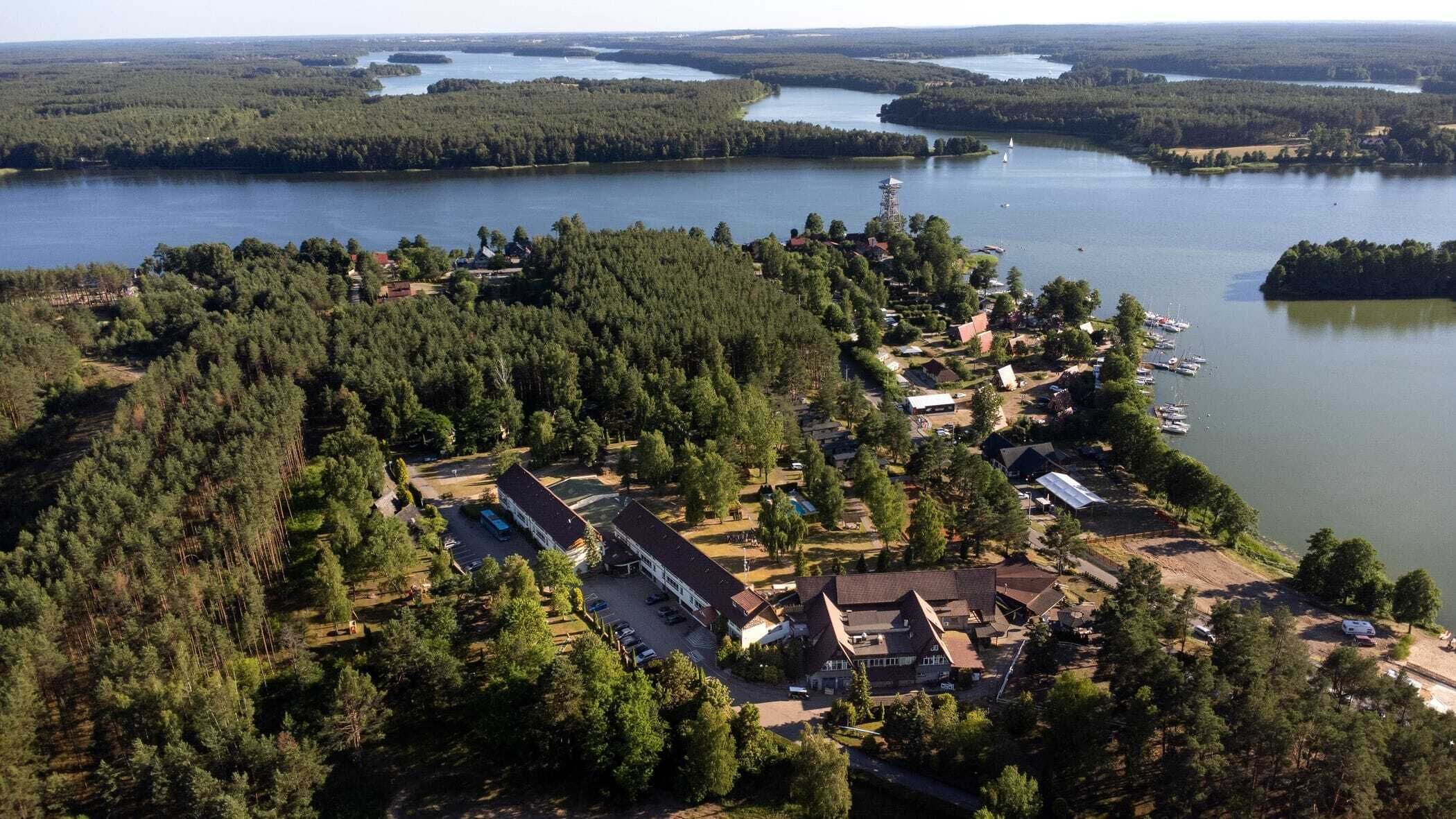 An aerial view of a lakeside property with multiple buildings, a marina, and surrounding forested areas.