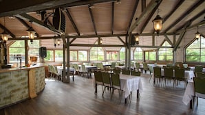 A spacious indoor dining area with wooden beams, tables with white tablecloths, and green chairs. - Hotel Niedzwiadek (Koscierzyna)