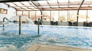 An indoor swimming pool with a water fountain feature, surrounded by seating areas and large windows. - Hotel Niedzwiadek (Koscierzyna)
