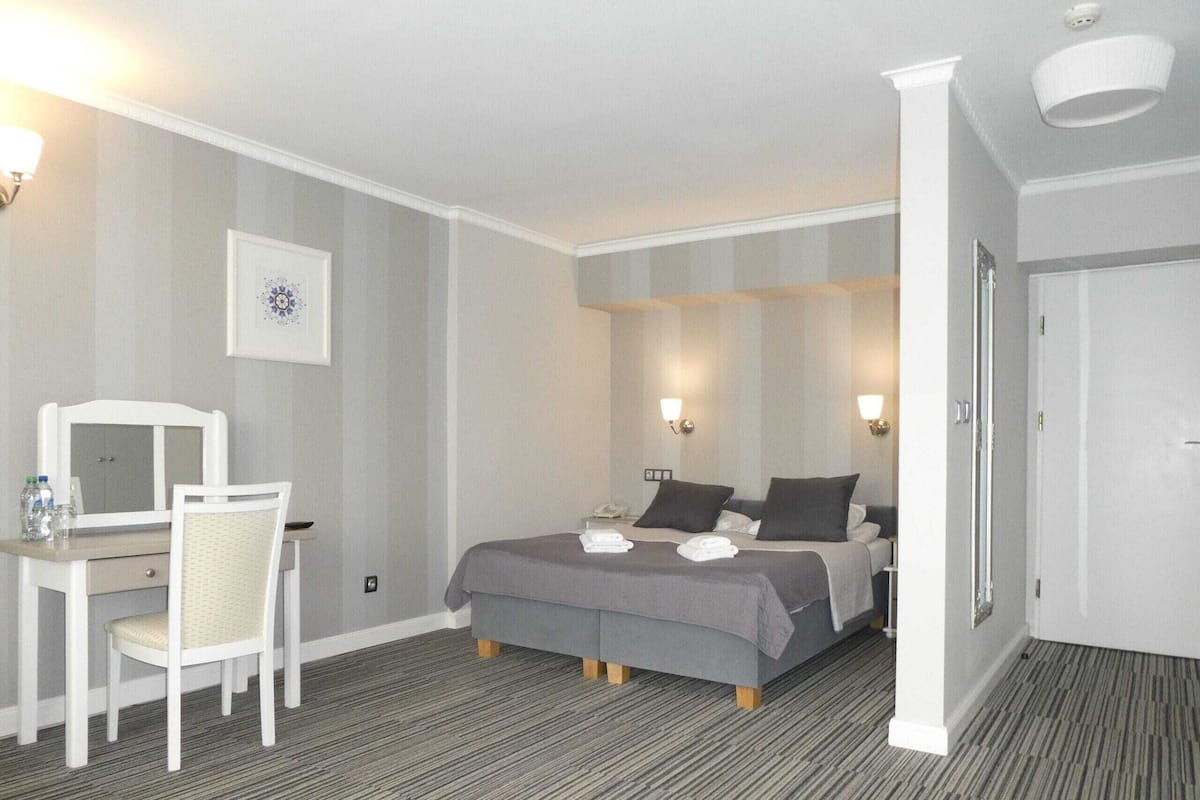 A hotel room with a bed, bedside table, chair, and a desk with a mirror.