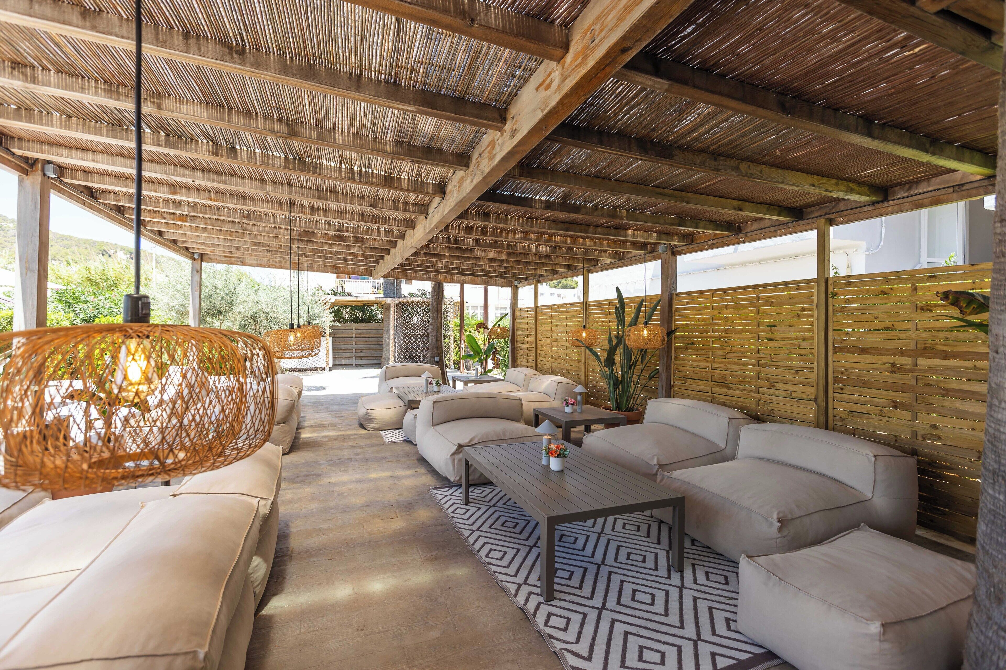 An outdoor lounge area with a high ceiling, wicker furniture, and a patterned rug.