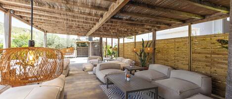 An outdoor lounge area with a high ceiling, wicker furniture, and a patterned rug.