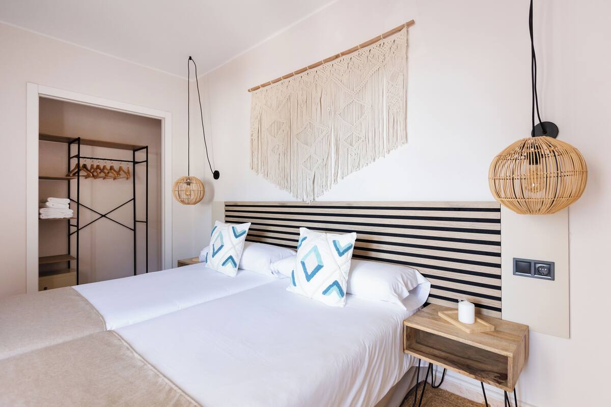 A neatly arranged bedroom with a bed, bedside tables, a hanging macrame wall piece, and a woven pendant light.