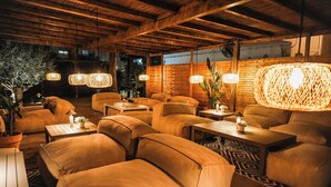 A cozy indoor seating area with cushioned sofas and tables, wooden ceiling beams, and hanging woven light fixtures. - SES VELES IBIZA HOUSE (Santa Eulalia del Rio)