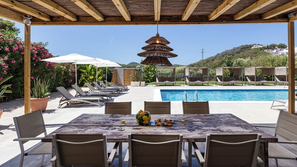 An outdoor pool area with a wooden pergola, lounge chairs, and a dining table with chairs. - SES VELES IBIZA HOUSE (Santa Eulalia del Rio)