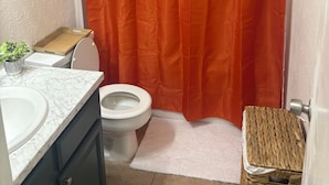 Une salle de bain avec des toilettes blanches, un lavabo blanc et un plateau en bois posé sur le comptoir.