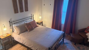 Un lit bien fait, avec une tête de lit, deux tables de chevet avec des lampes, un tapis à motifs et une fenêtre avec des rideaux.