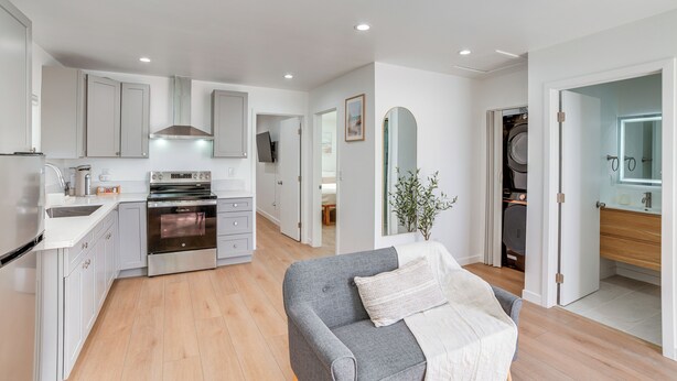 Una cocina moderna con armarios blancos, un horno empotrado y una zona de comedor con un sofá gris.