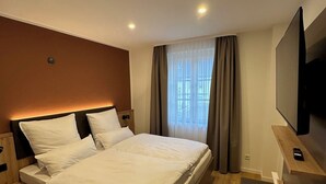 A modern hotel room with a large bed, a flat-screen TV, and a wooden bench. - Apartment Ahrblick (1-4 persons) | Top vacation apartment with a view of the Ahr (Altenahr)