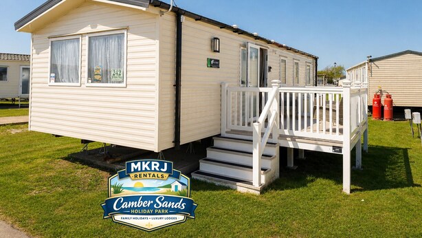 Une maison mobile dotée d’une terrasse, d’une antenne parabolique et d’une enseigne indiquant « MKRJ Rentals », située dans le parc de vacances de Camber Sands.
