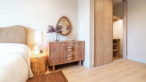 Une chambre à coucher comprenant un lit, une table de chevet, une commode en bois, un miroir et un placard avec des portes coulissantes.