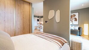A modern bedroom with a large bed, a wardrobe, a dining area in the background, and a grey sofa. - Chic Urban Escape - Studio Apartment, Sleeps 2 (London)