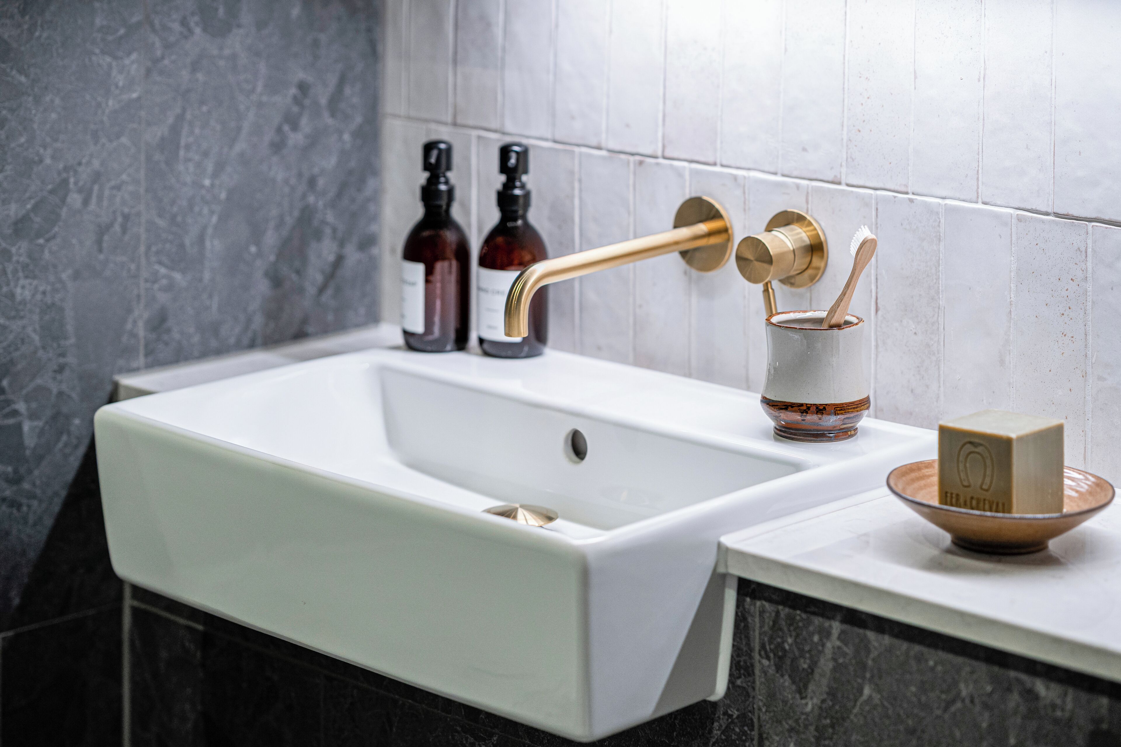 Een badkamer met een wit wastafel, een gouden kraan en twee zeepdispensers.