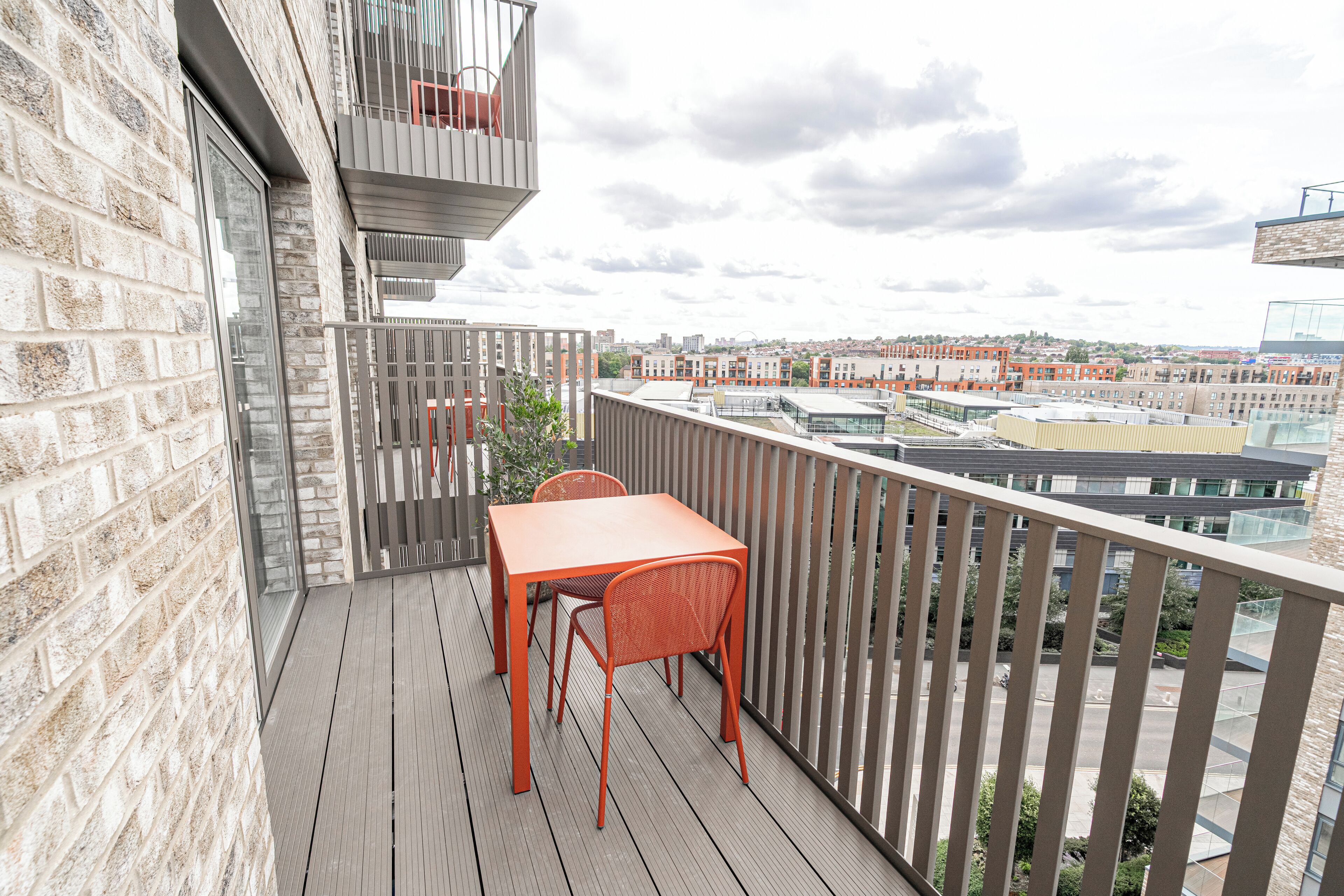 Een balkon met een houten tafel en stoelen, een bakstenen muur en uitzicht op een stadsbeeld.