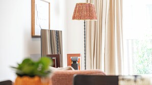 A hotel room with a bed, a desk, a lamp, a potted plant, and a window with curtains. - Light and Space Retreat (London)