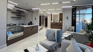 A modern hotel lobby with a kitchen area, seating arrangements, and a view of the city. - Aswar Plus for serviced apartments (Tabuk)