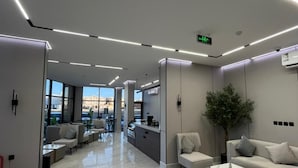 A modern hotel lobby with a clean, minimalist design, featuring a reception desk, seating areas, and a large window offering a view of the cityscape. - Aswar Plus for serviced apartments (Tabuk)