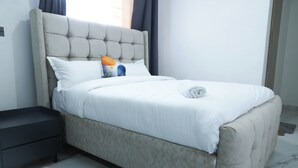 Ein Bett mit einem gepolsterten Kopfteil, weißer Bettwäsche, einem kleinen Nachttisch und einem gemusterten Teppich.