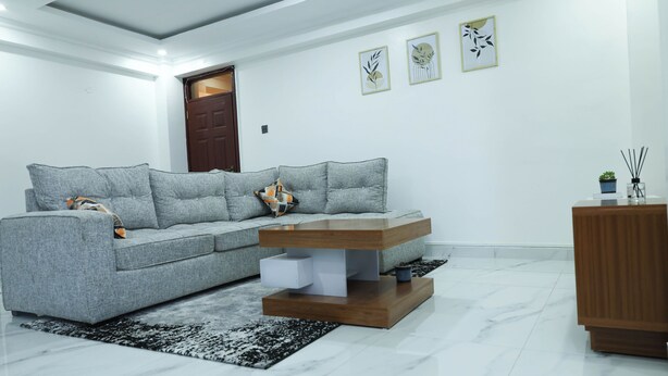 Un salon moderne avec un canapé d’angle gris, une table basse en bois et un tapis noir et blanc.