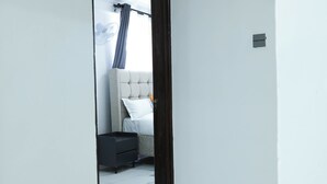 Un couloir menant à une chambre à coucher équipée d’un lit, d’une table de chevet et d’un ventilateur fixé au mur.