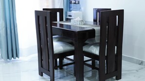 Un espace repas avec une table et des chaises en bois foncé, un distributeur d’eau et un sol en marbre.