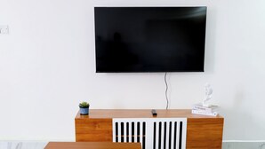 Un salon moderne avec une table basse en bois, un canapé blanc, un meuble TV en bois avec un téléviseur à écran plat et une petite plante.