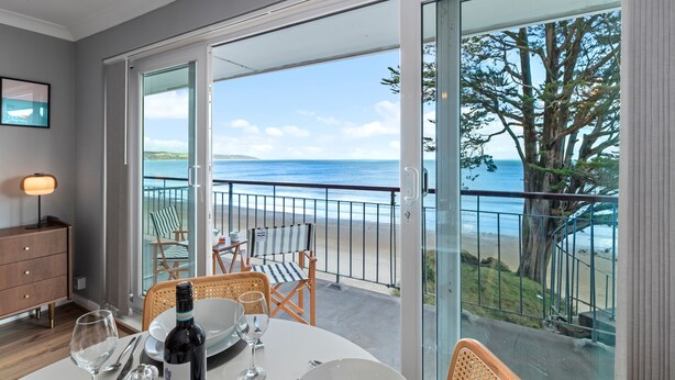 Un balcon avec une table dressée pour le dîner, offrant une vue sur une plage et l’océan.