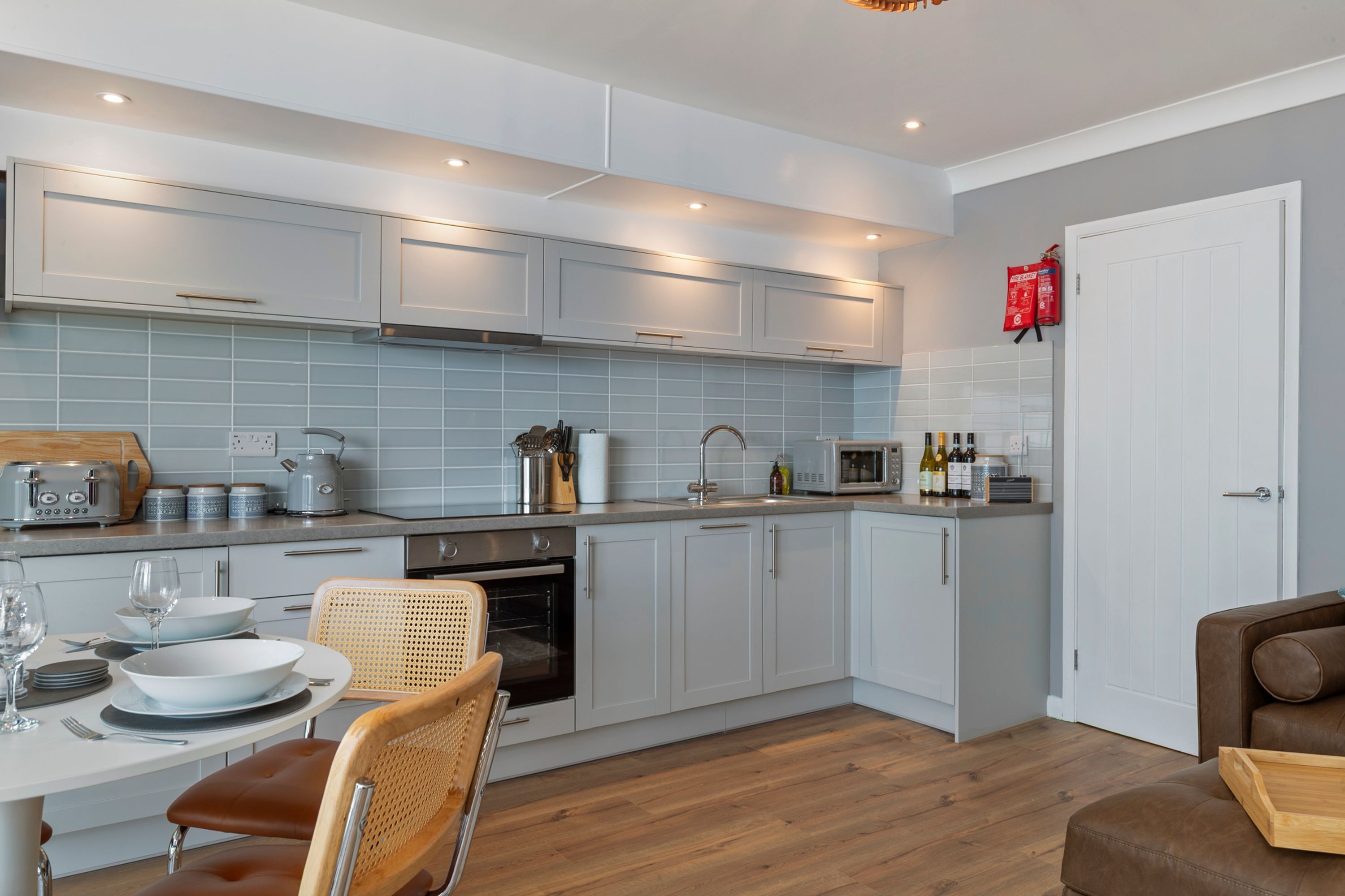 A modern kitchen with white cabinets, a dining area with a table and chairs, and a wooden floor.