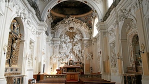 Interior de igreja ricamente decorado, com altos tetos, frescos detalhados e um altar central.