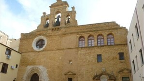 Um edifício histórico com uma torre de sino, janelas em arco e um portal central.