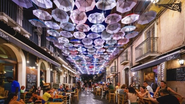 Calle con mesas y sillas, gente sentada y caminando.