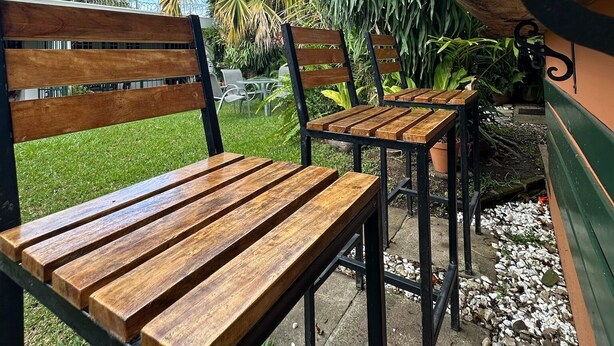Een terras met houten banken en tafels, omringd door groen en een heldere lucht.