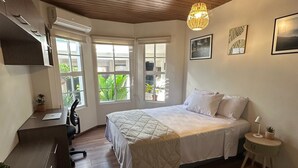 Een slaapkamer met een bed, een bureau, een stoel, een klein tafeltje en een hanglamp.