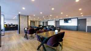 A conference room with round tables and purple chairs, equipped with coffee machines and a projector screen. - Venesia Hotel (Arsin)