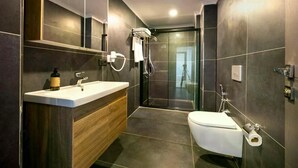 A modern bathroom with a large mirror, a wooden vanity, a white sink, a toilet, and a glass-enclosed shower. - Venesia Hotel (Arsin)